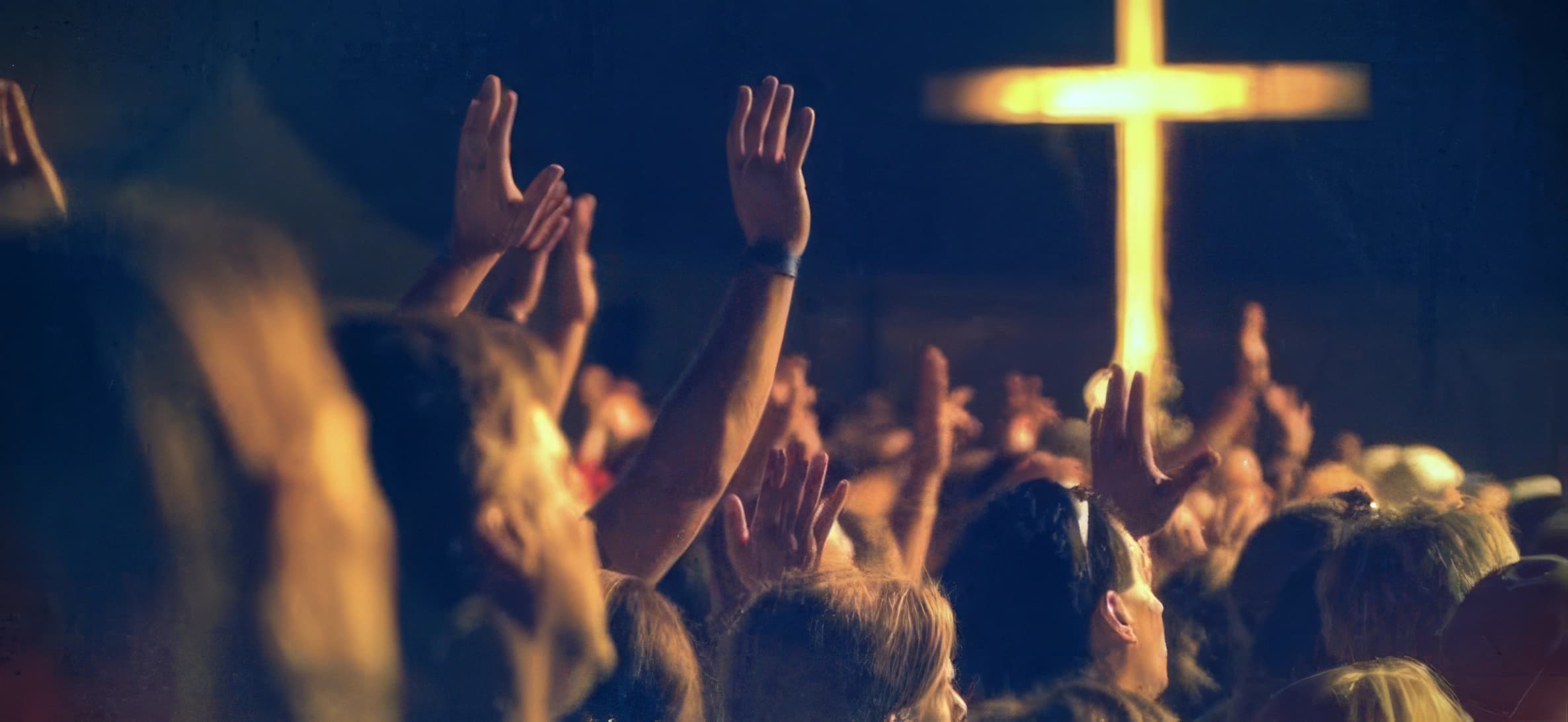 Worshippers raising their hands toward an illuminated cross